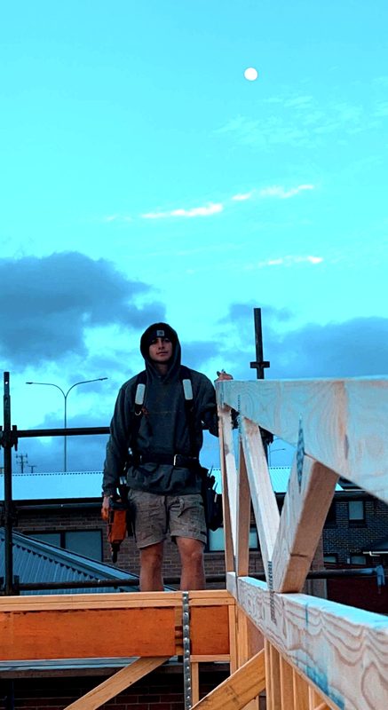 Kyle standing on a house frame at dusk, nail gun in hand