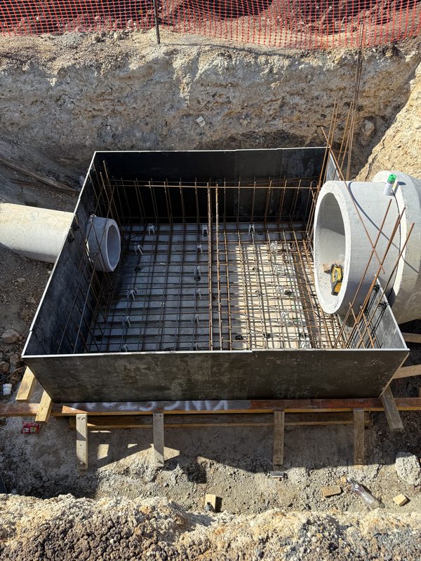 Boxed stormwater pit formwork with film-faced ply forms and base reinforcement, pipe penetration visible.