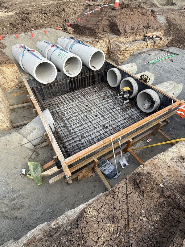 Steel reinforcement mesh on bar chairs across a pit base with pipe penetrations set, ready to pour.