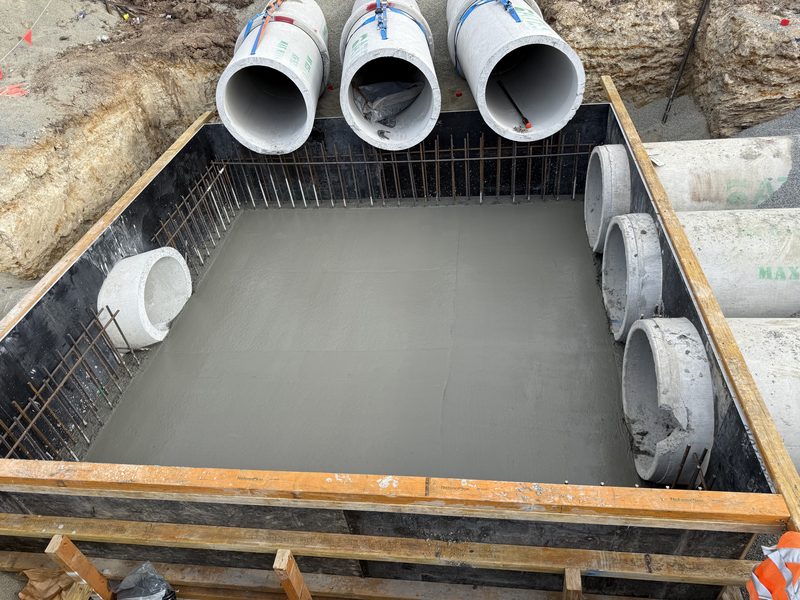 Freshly poured and floated pit base slab with pipe penetrations and starter bars for the walls.