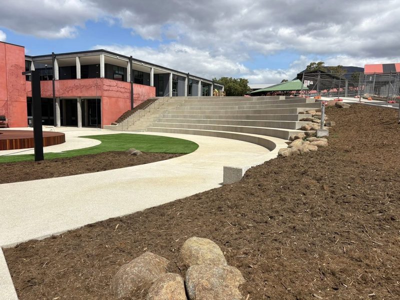 Curved concrete amphitheatre with tiered seating and stone edging, poured in place.