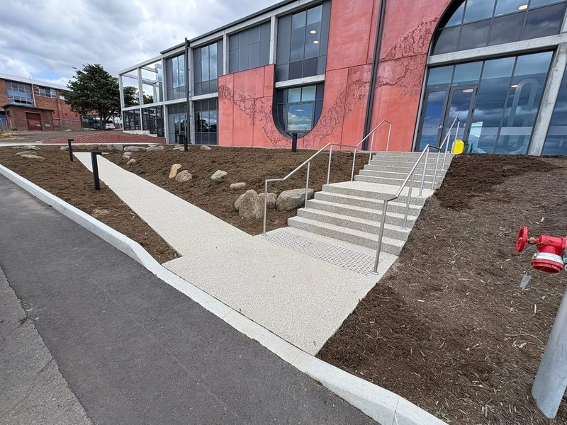 Concrete entry stairs with steel handrails meeting a curved exposed-aggregate path.