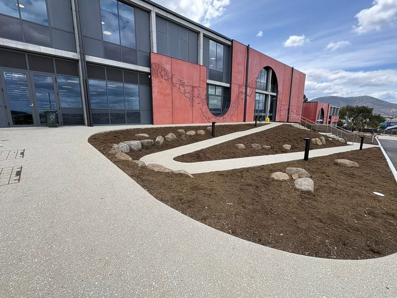 Curved mulched garden beds edged with winding light-aggregate paths outside a commercial building.