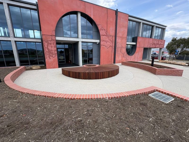 Circular hardwood bench platform at the main entry, ringed by curved brick edging.