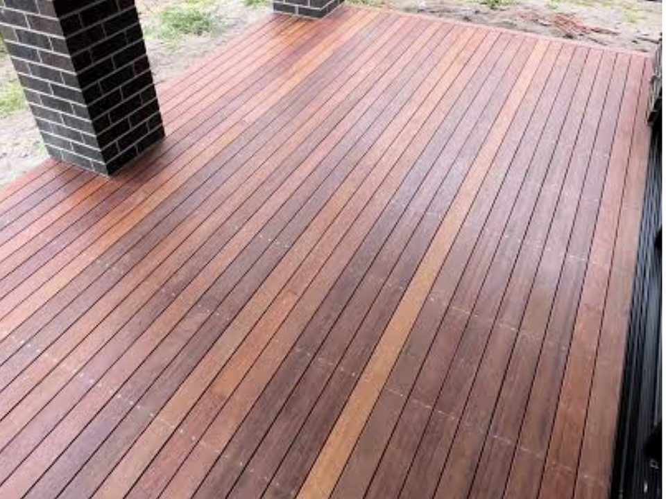 A rich red-brown freshly finished hardwood deck with dark brick piers rising from it, viewed from above.