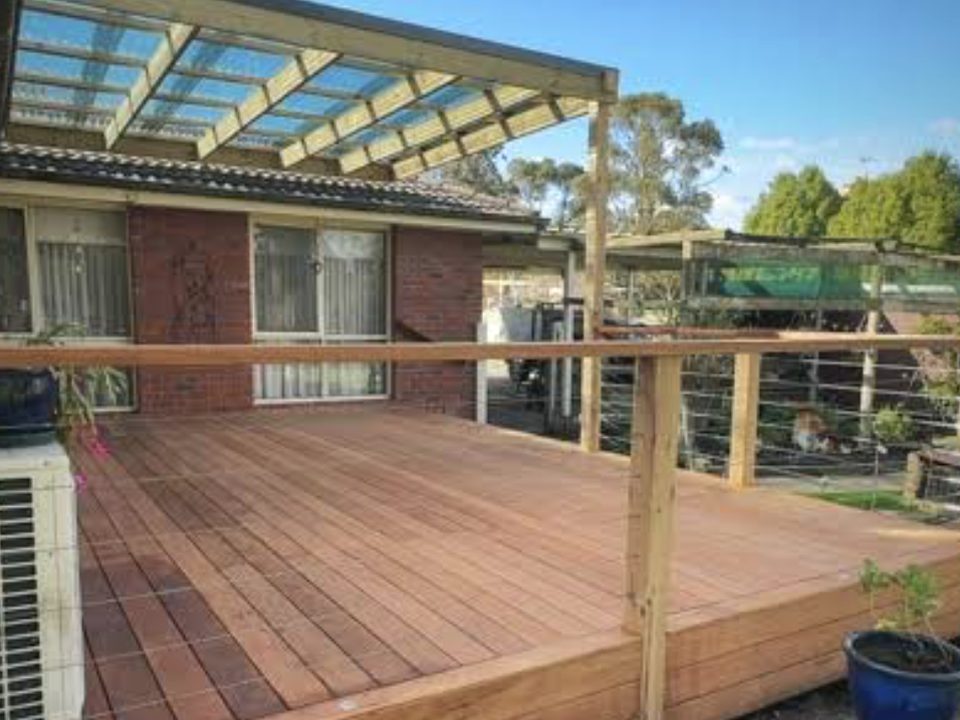 Elevated hardwood deck with a polycarbonate pergola roof, wire balustrade and timber handrail against a brick home.