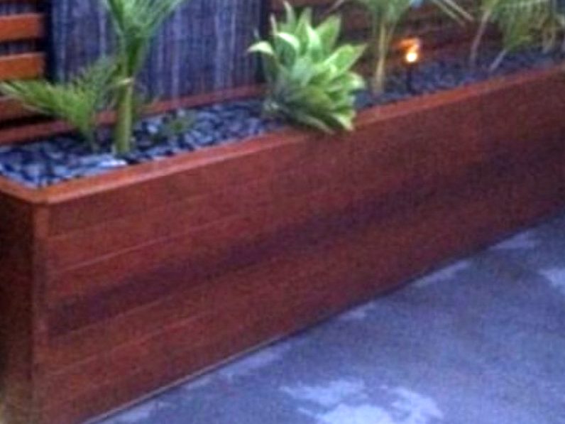 Finished stained timber planter box filled with plants and pebbles, lit at night.